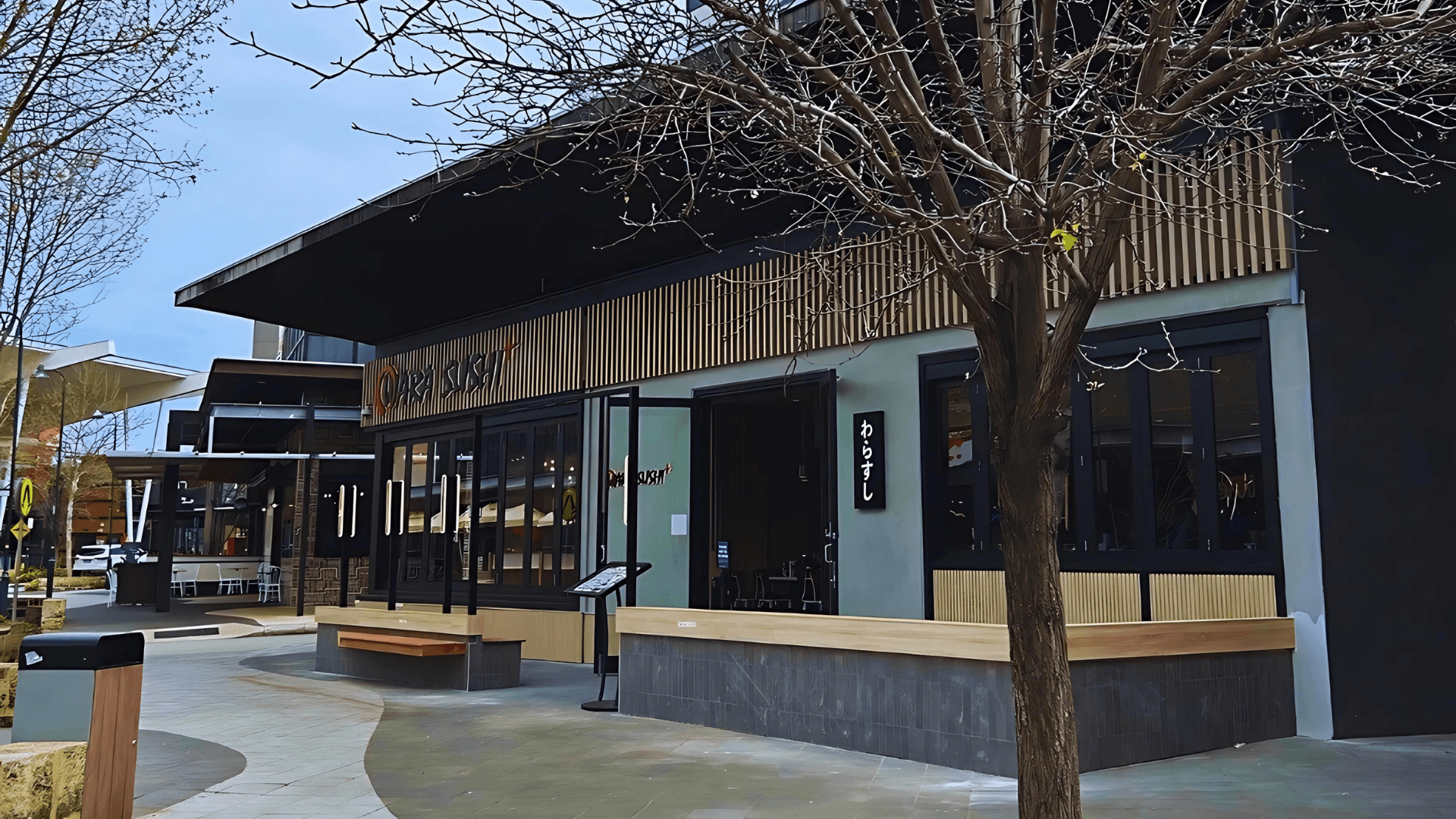 A wood panelled sushi restaurant with outdoor dining in a shopping centre dining precinct